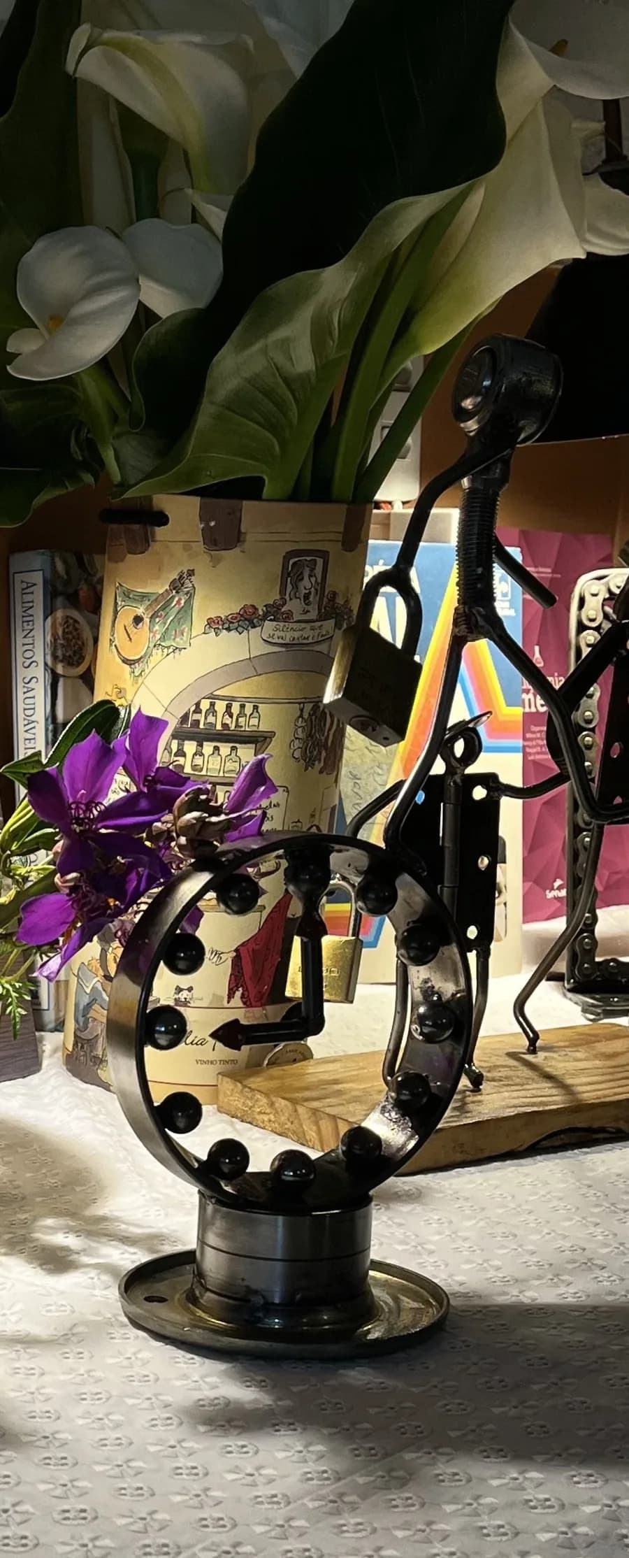 Escultura de figura humana sobre aro de rolamento, feita de porcas e mancais — obra de Cláudio Silveira, exposição no Bistrô Chef Lau, Muzambinho/MG — foto real